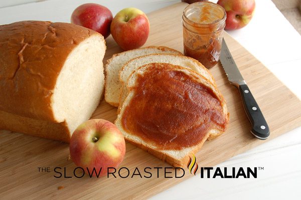 Crockpot apple butter spread onto slice of white bread next to loaf of bread