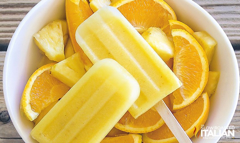 pineapple orange popsicles in white bowl with orange wedges
