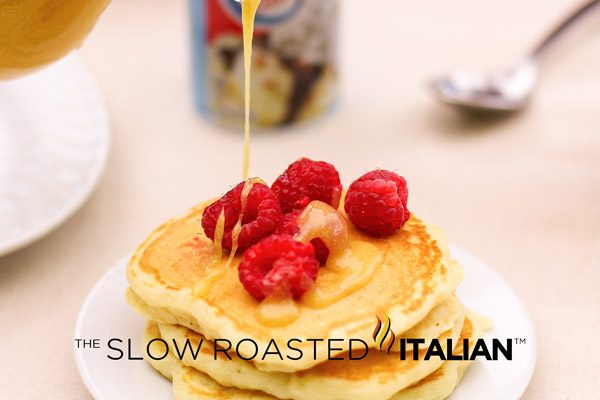 pouring syrup onto stack of fluffy pancakes