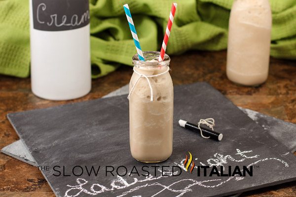 chocolate caramel milkshake in glass bottle with 2 straws sitting on a chalkboard