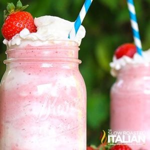 creamy strawberry shake in tall mason jar with whipped cream and straw.