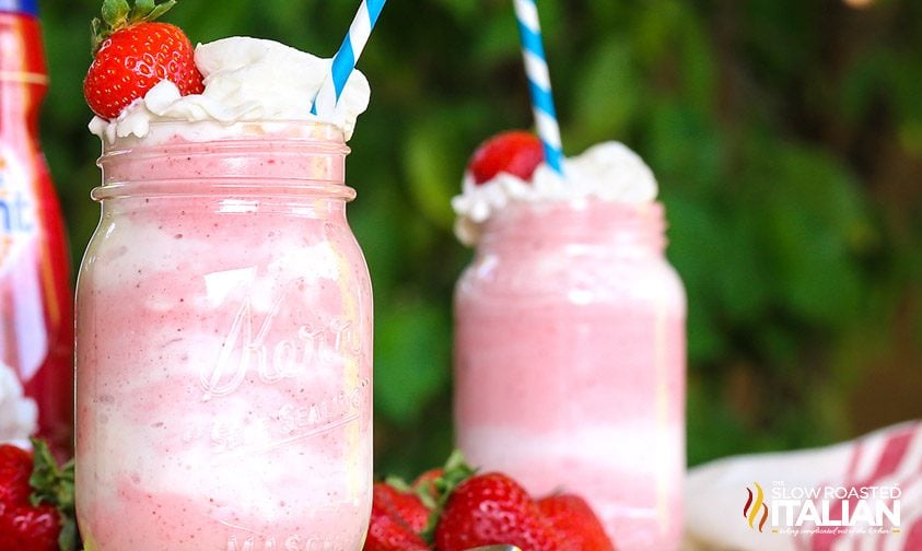 two frozen strawberry drinks topped with whipped cream and red berries.