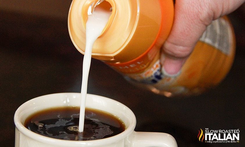 pouring creamer into cup of coffee