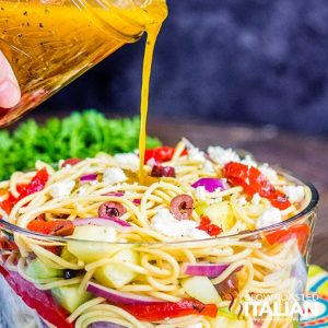 Greek Spaghetti Salad in a clear bowl with dressing on top