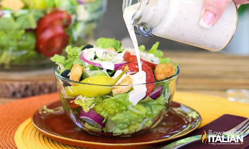 pouring white salad dressing on salad