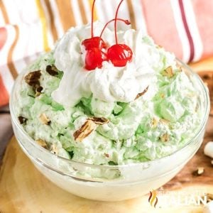 bowl of pistachio fluff topped with whipped cream and maraschino cherries