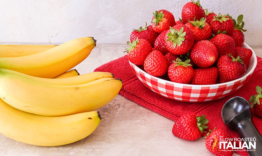 bunch of ripe bananas next to bowl of fresh strawberries