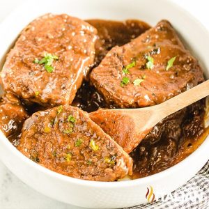spooning brown gravy onto meat in a serving dish.