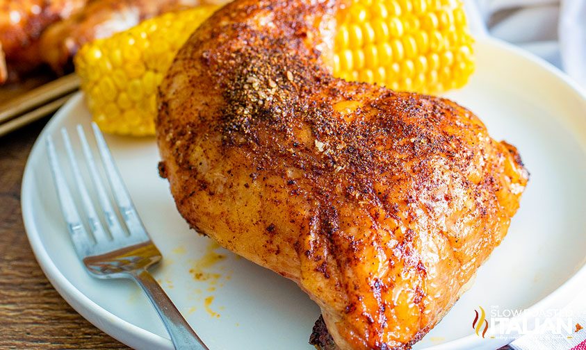 smoked chicken quarters on a white plate with corn on the cob and a fork