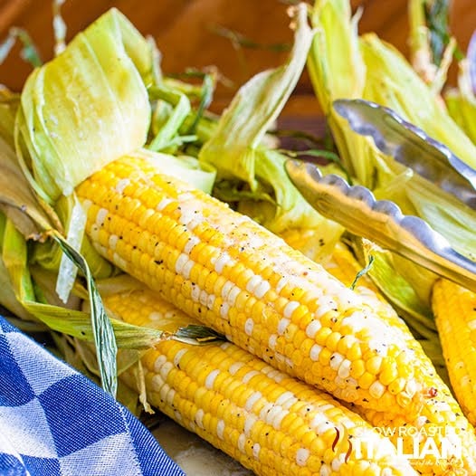 tongs picking up smoked corn on the cob