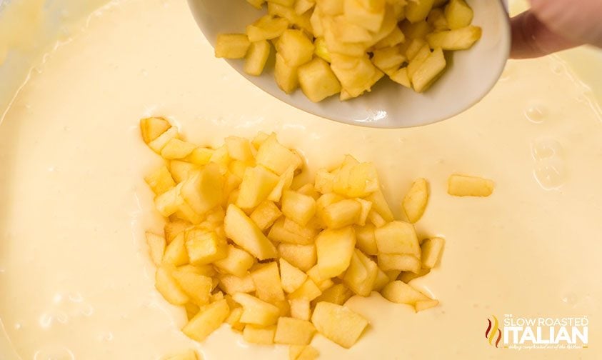 apple chunks being poured into cheesecake batter
