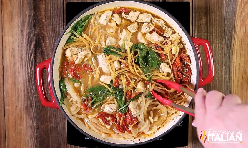 using tongs to stir garlic chicken pasta