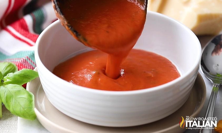 Ladling tomato basil soup into a white bowl