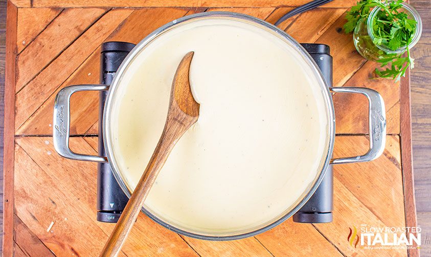overhead: creamy white cheddar cheese sauce in pot with wooden spoon