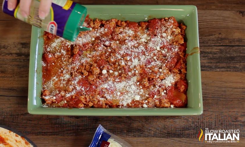pouring parmesan cheese on top of lasagna