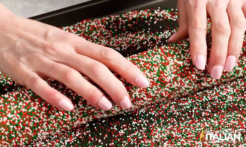 woman's hands rolling sweet pastry dough through red and green sprinkles