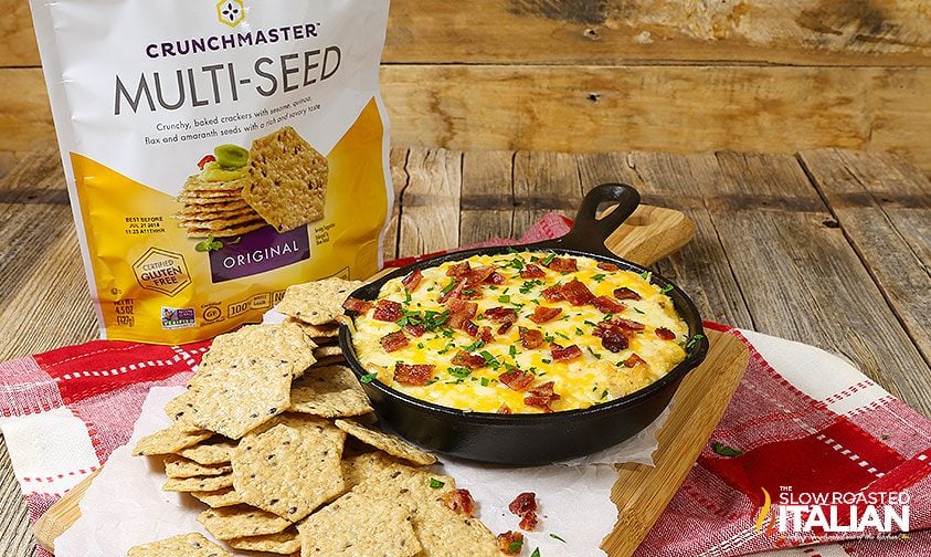 pile of multigrain crackers next to individual size skillet of cheesy dip