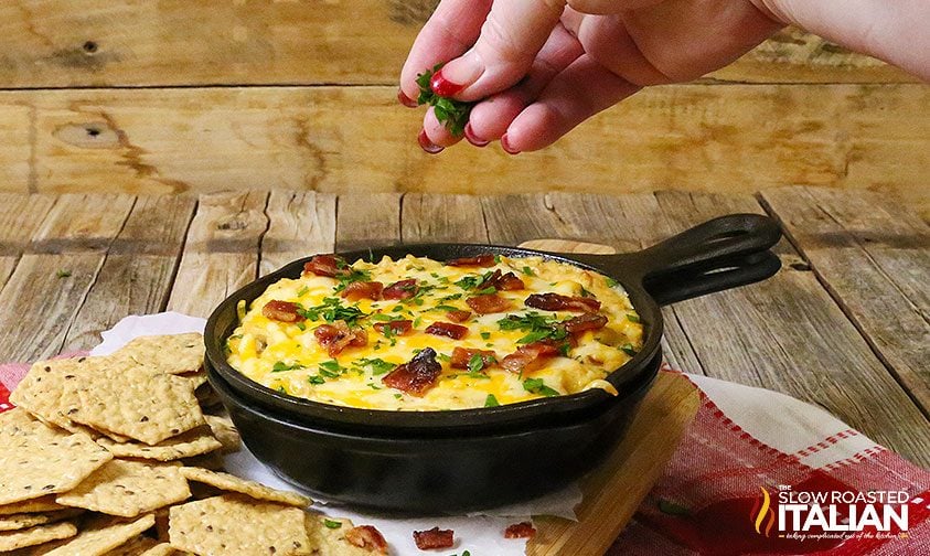 sprinkling cilantro garnish on jalapeno popper dip in cast iron skillet