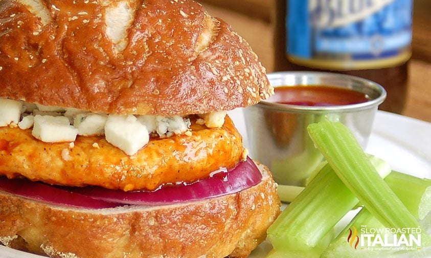 close up image of grilled chicken sausage patty on pretzel bun with spicy sauce and blue cheese crumbles