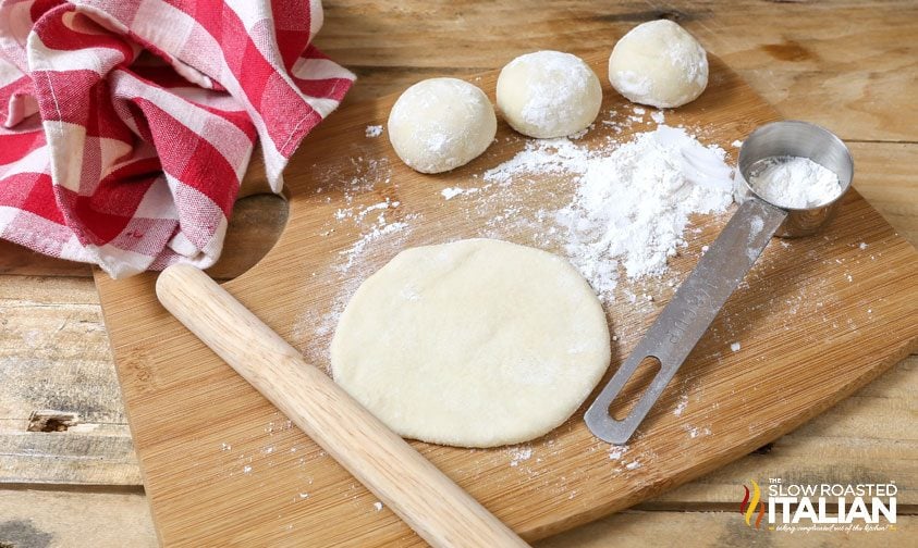 balls of bread dough on counter; one flattened with rolling pin