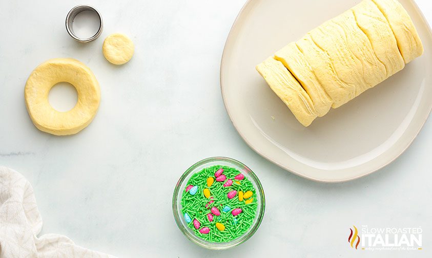 overhead: biscuit cutter and pillsbury biscuits dough next to bowl of easter sprinkles