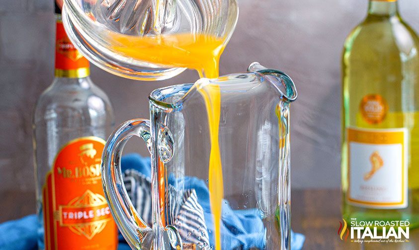 pouring orange juice into a pitcher for sangria recipe