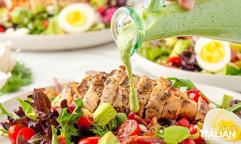pouring green goddess salad dressing over fresh salad and grilled chicken