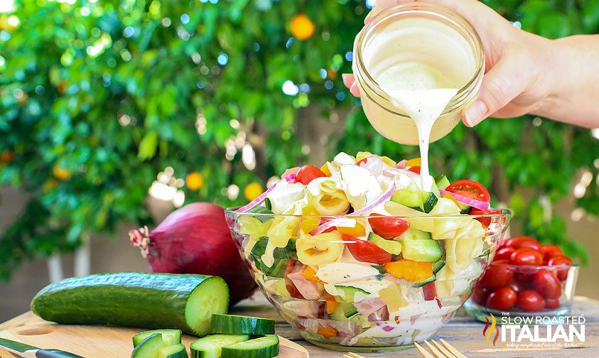 pouring dressing over tortellini salad