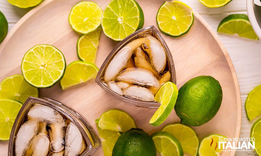 overhead: lime slices surrounding drinking glasses with ice and dark liquid