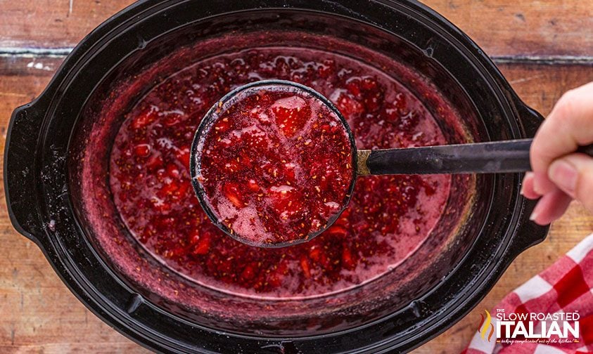 mixed berry jam on a ladle in a slow cooker