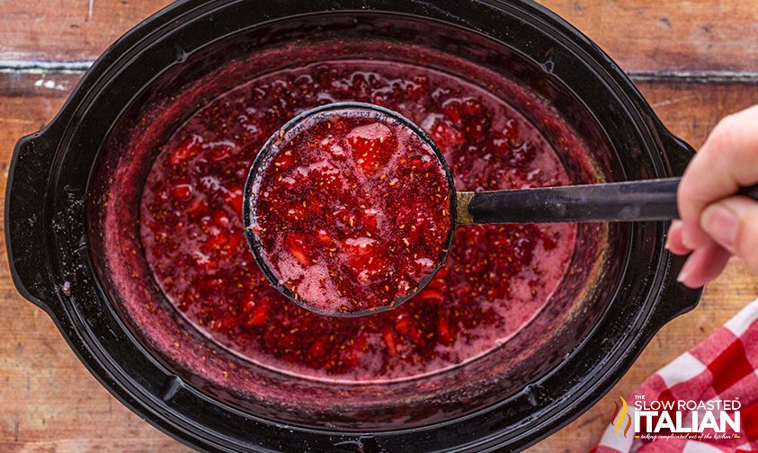 mixed berry jam on a ladle in a slow cooker