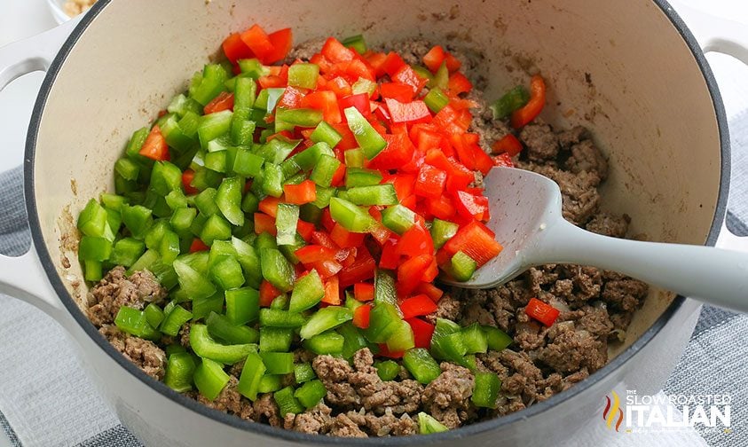 combining cooked ground beef with diced red and green bell peppers in bowl