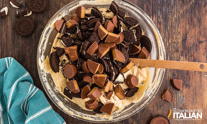 stirring chocolate cookies and peanut butter cups into cheesecake salad