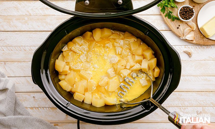 crock pot mashed potatoes being mashed in the slow cooker