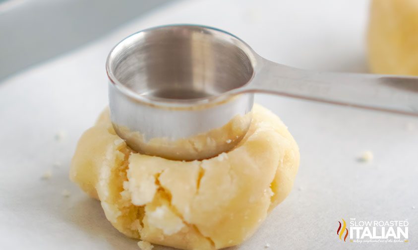 using measuring cup to make divot in cookie dough