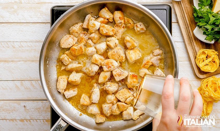 pouring white wine into skillet with diced pieces of white meat