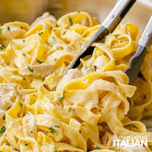 serving chicken alfredo with metal tongs