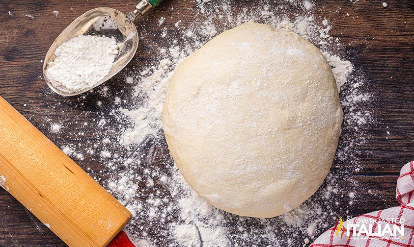 pizza dough dusted with flour on wooden board