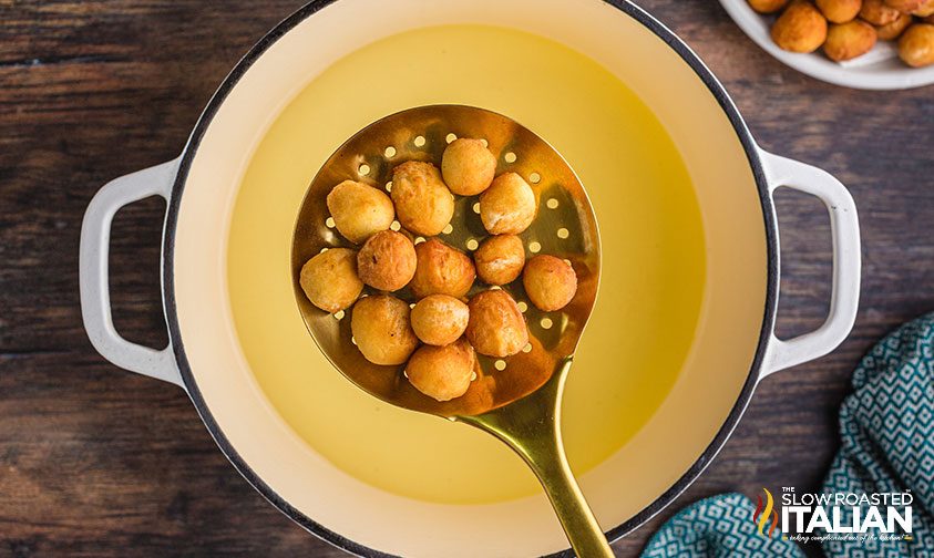 fried dough balls on a straining spoon