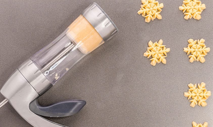 pressing spritz cookies onto baking sheet