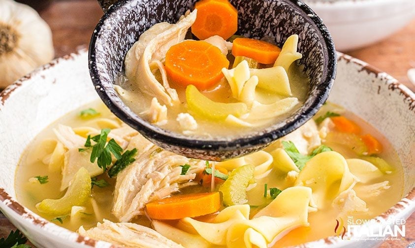 ladle of homemade soup with noodles, carrots and white meat
