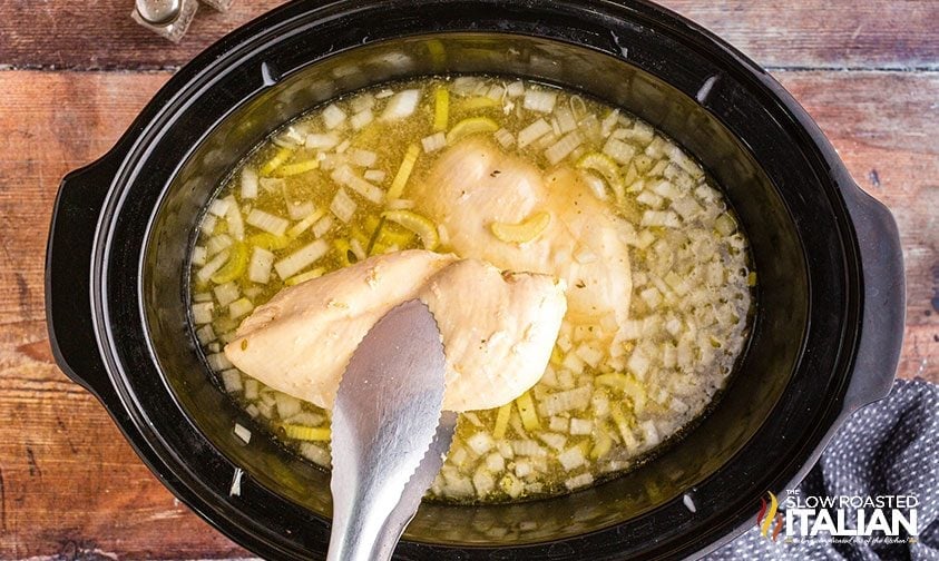 adding chicken breast to a crockpot for homemade soup