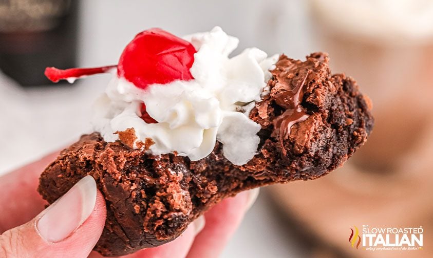 woman's hand holding boozy brownie topped with whipped cream
