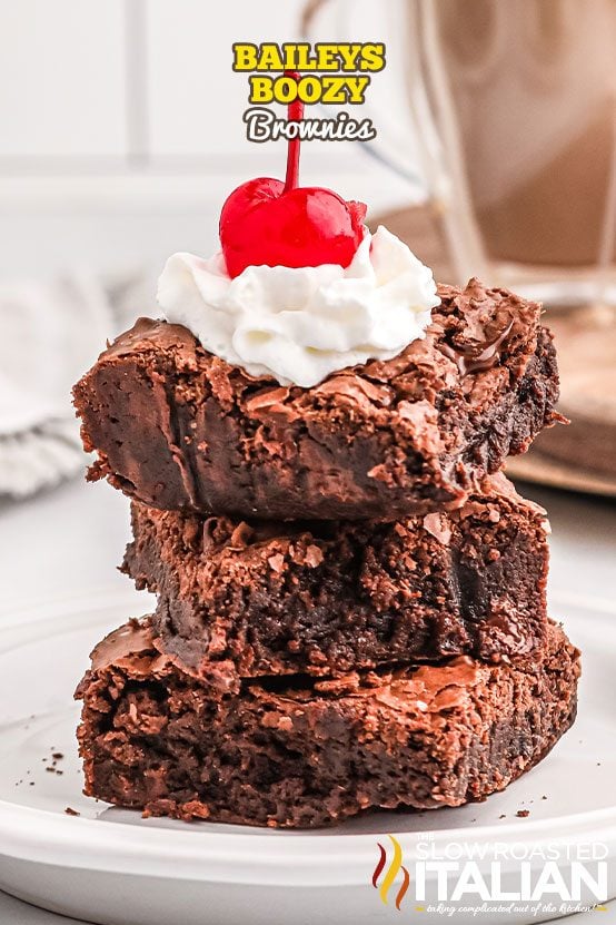 stack of boozy brownies topped with whipped cream and a cherry