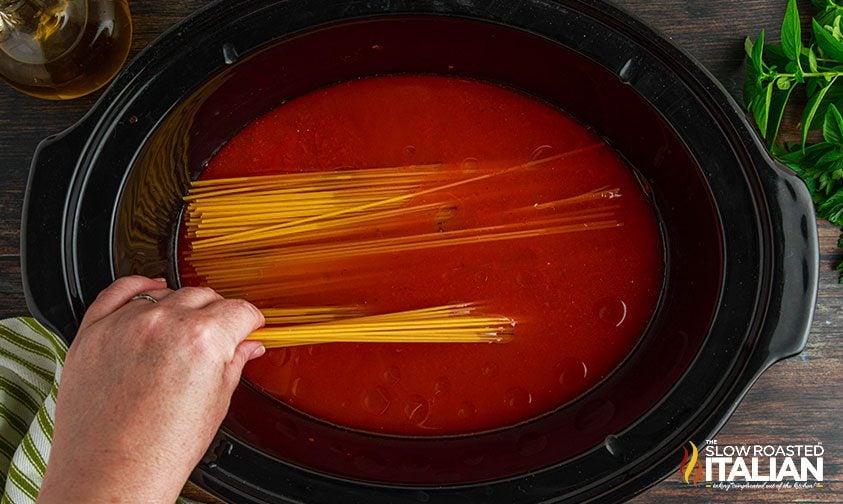 placing spaghetti in crockpot with red sauce