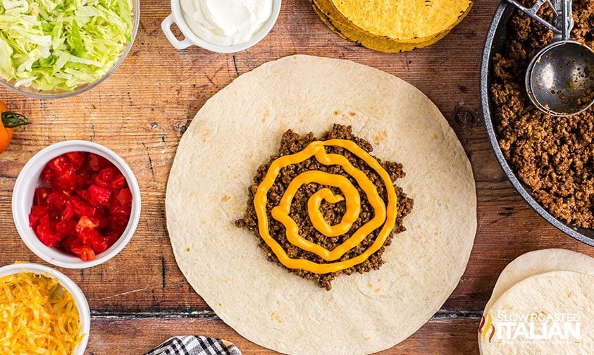 overhead: ground beef and nacho cheese sauce on flour tortilla