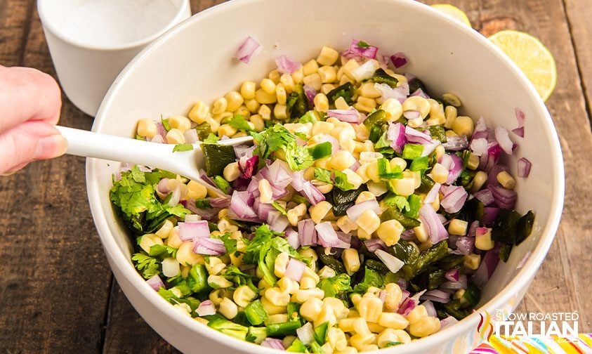 stirring to combine green chiles, red onion, cilantro and corn in white bowl