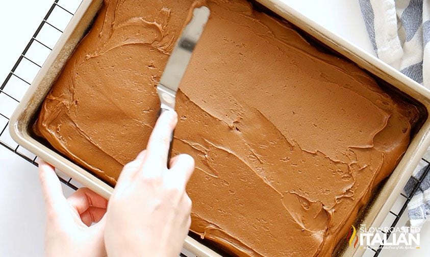 spreading chocolate frosting on a snack cake