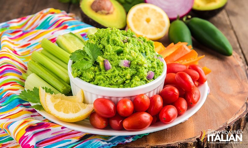 healthy guacamole on a serving plate with veggies for dipping