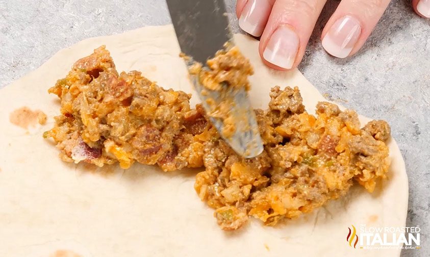 spreading spicy beef mixture on flour tortilla